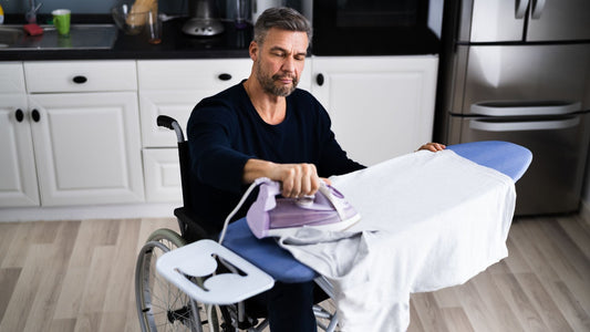 A wheelchair user uses an iron to iron a Tshirt in a kitchen