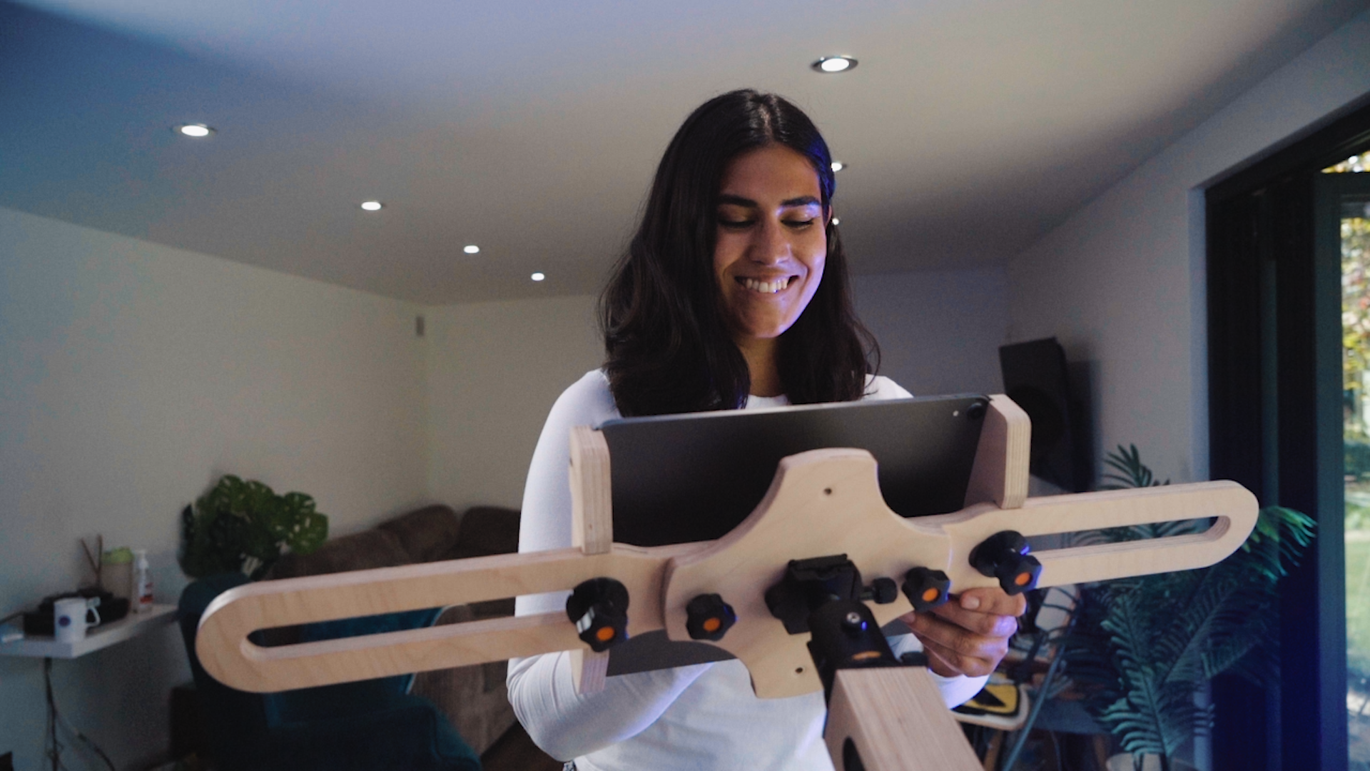 A woman with shoulder length dark hair is standing in front of a freasel. She smiles and looks at an Ipad on the freasel as she draws.