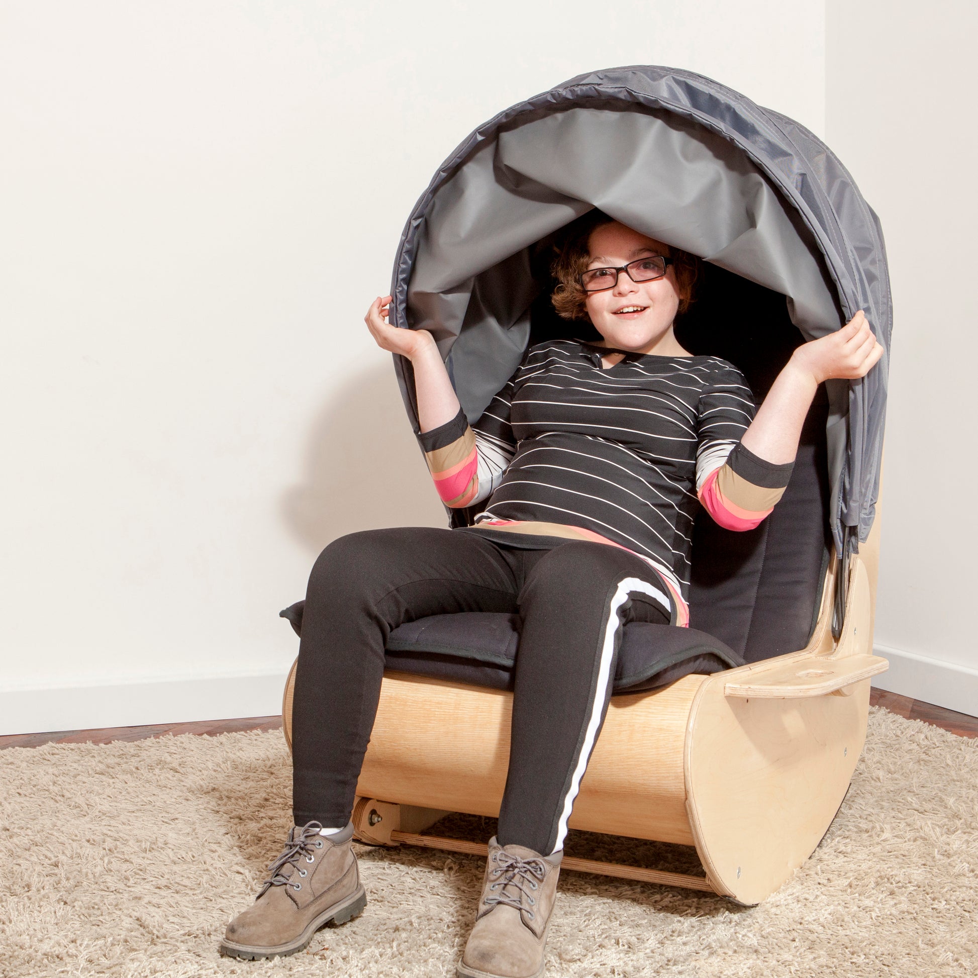 Teenager sits in sensory shell rocking chair with hands on hood to pull it down