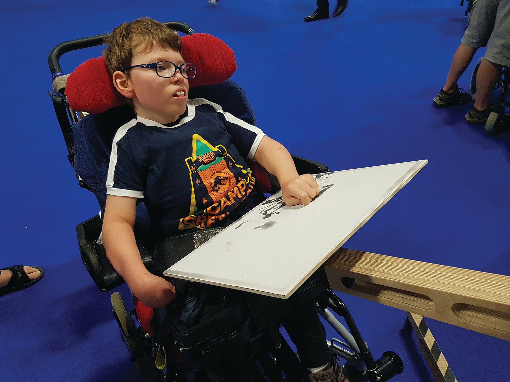 A young person in a postural wheelchair sits with a canvas on the freasel on their lap