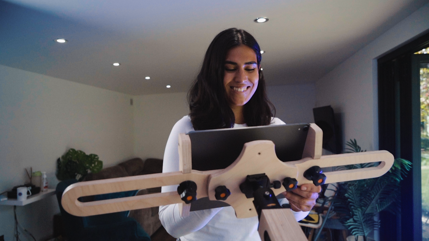 A woman with shoulder length dark hair is standing in front of a freasel. She smiles and looks at  an Ipad on the freasel as she draws. 