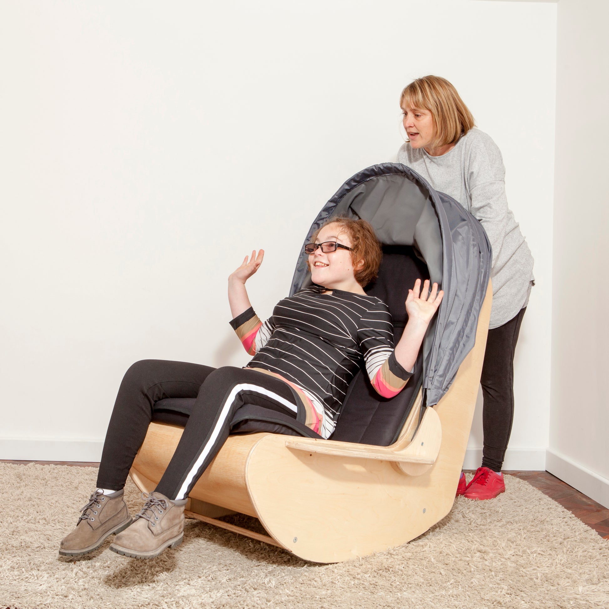 Teenager is rocked in the sensory shell chair by an adult holding the rear handles