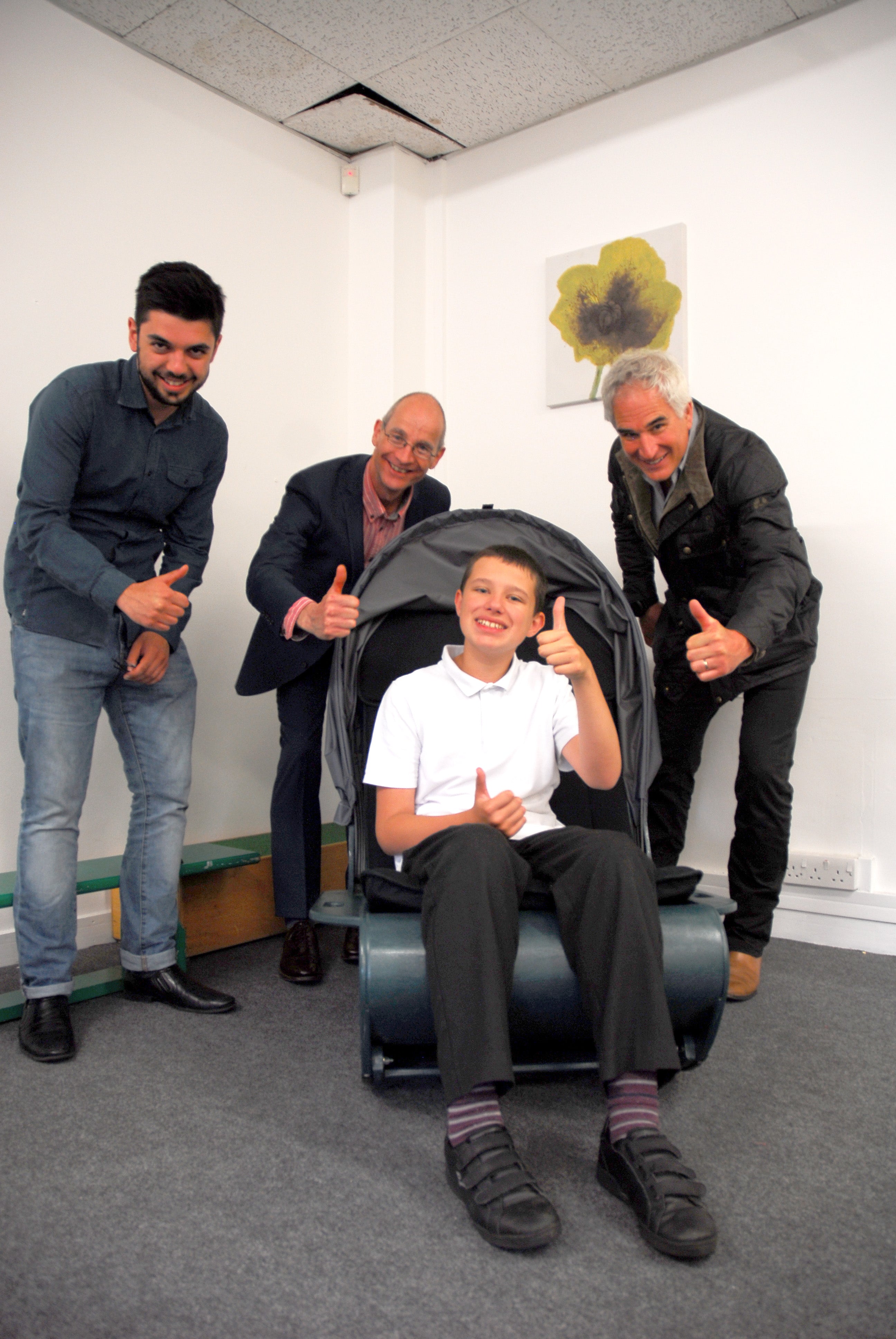 A child in school uniform sits in the sensory chair giving a thumbs up. Three adults also are in the picture giving thumbs up